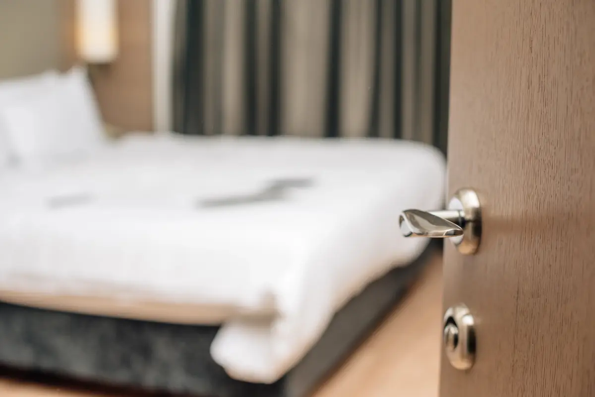Porte entrouverte sur une chambre d’hôtel avec un grand lit blanc